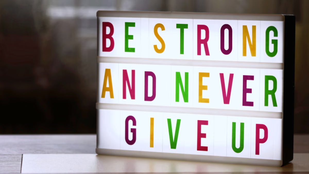 Motivational lightbox sign displaying 'Be Strong and Never Give Up.'